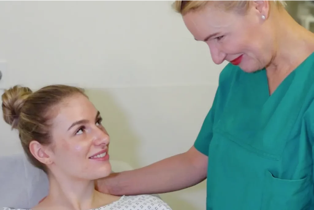 Aufnahme von Dr. Berkei, die neben einer sitzenden Patientin steht und ihr die Hand auf die Schulter legt. Beide im OP-Kleidung.